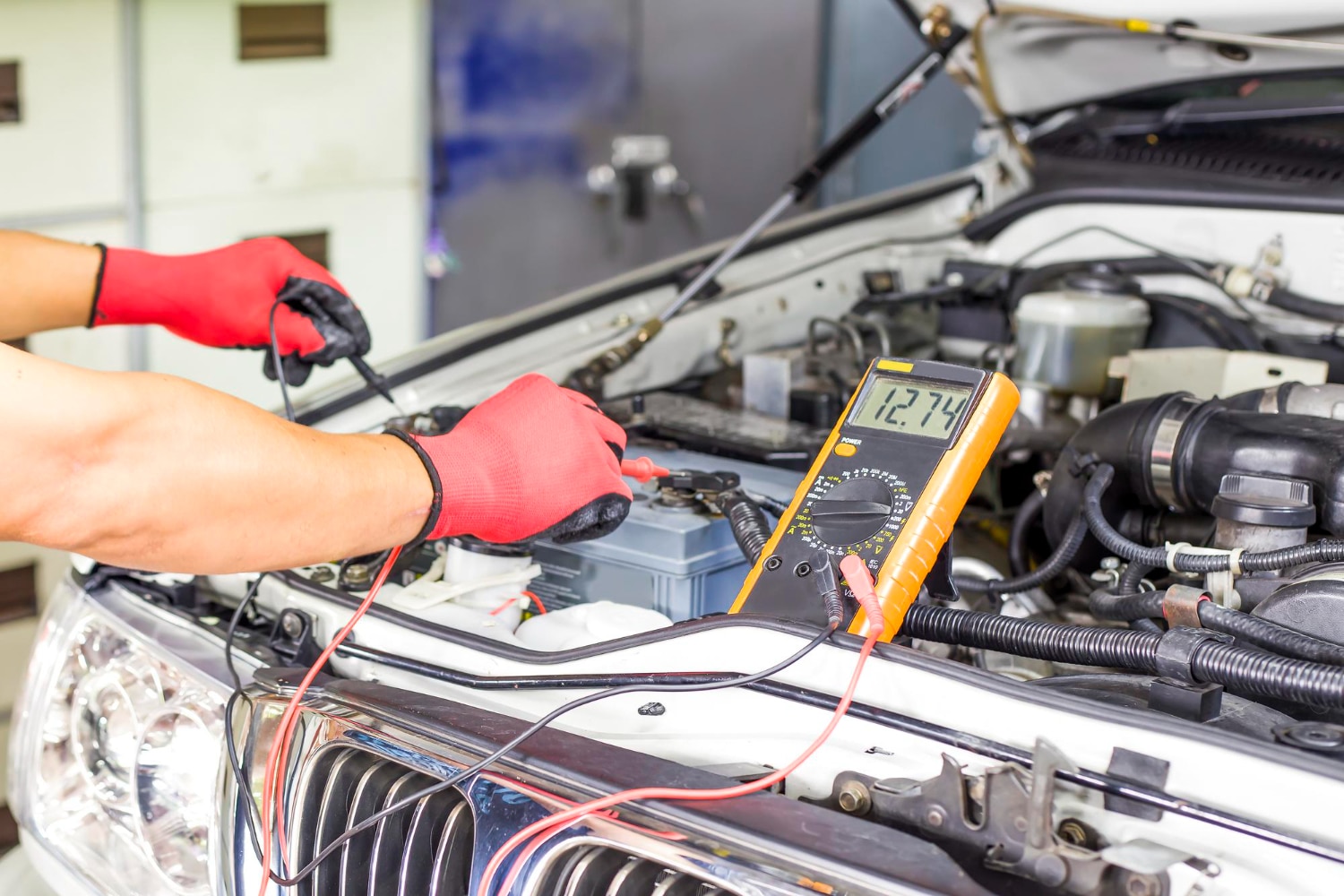 Mechanic testing a car battery with a digital multimeter.