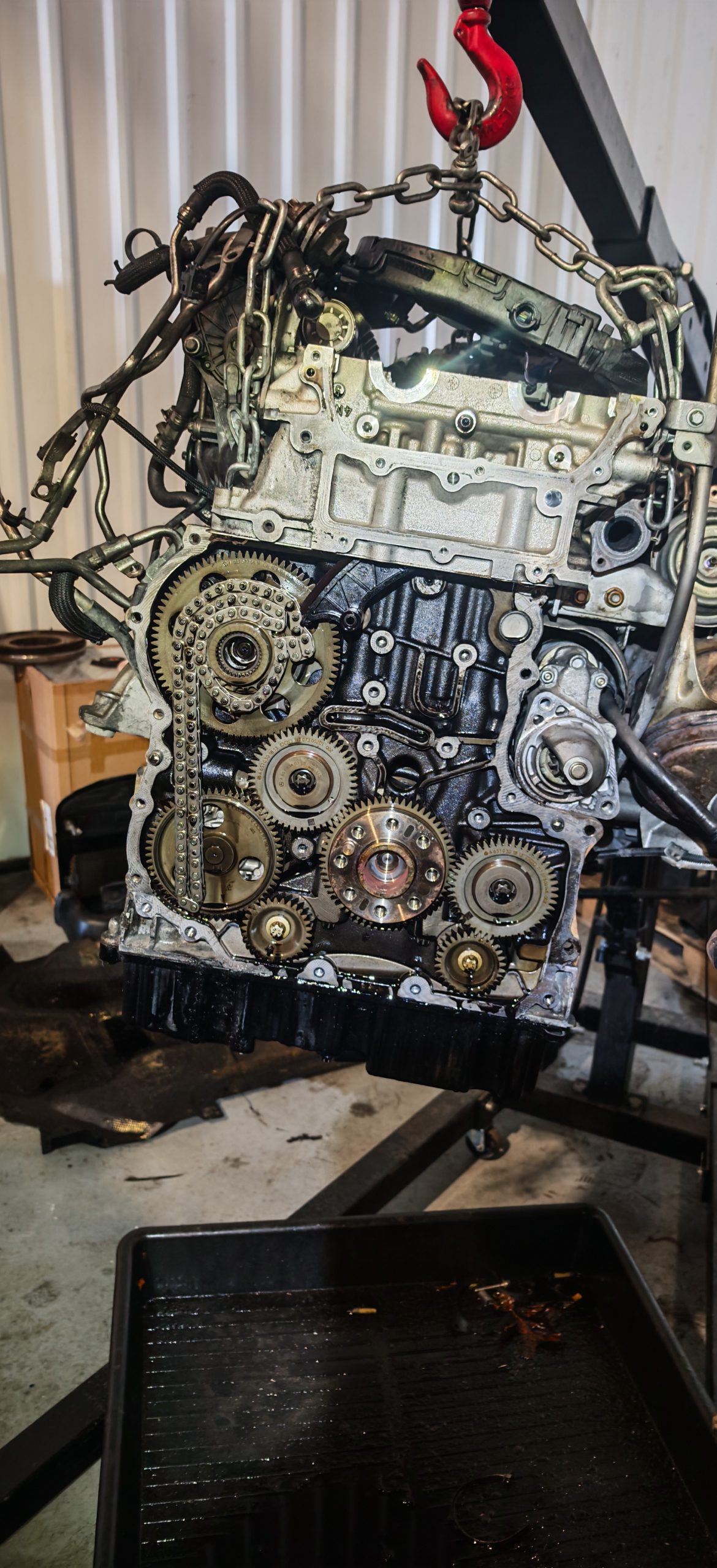 Removed car engine suspended by a hoist with exposed timing gears during repair.
