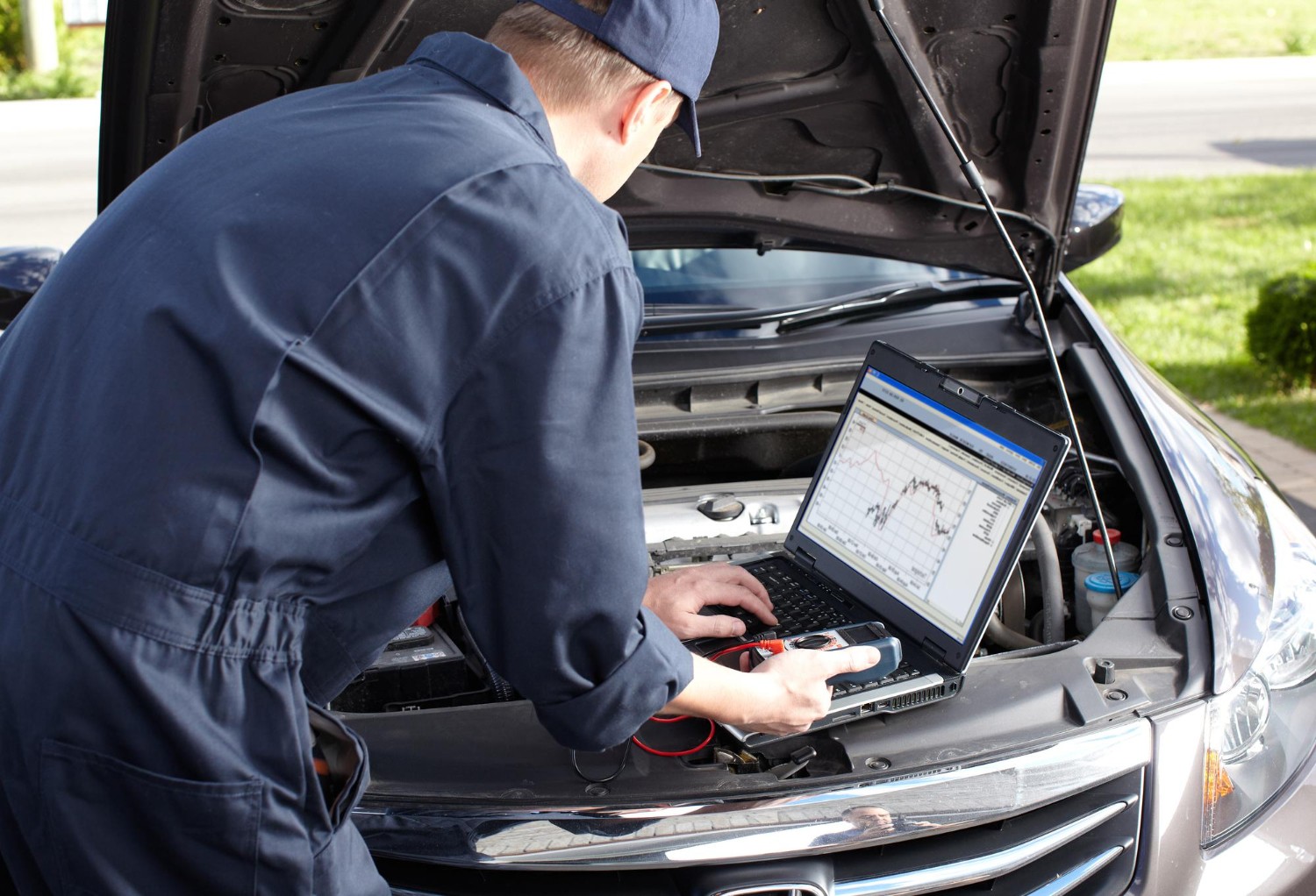 Car mechanic testing vehicle electronics with a diagnostic laptop connected under the open hood